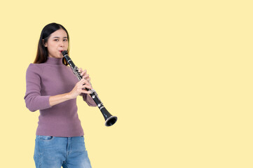 A talented Asian woman is playing a clarinet while standing against an isolated yellow background.