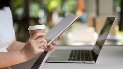 A female freelancer managing her work, sipping coffee, sitting in a coffee shop with her laptop.