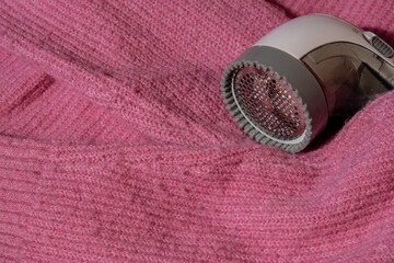 Anti-pilling razor. Device for shaving clothes. Anti-Plush fabric Shaver. Electric portable sweater pill defuzzer Lint remover from pink acrylic or wool sweater. Electric device fabric shaver after