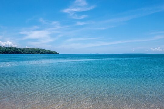 A beautiful calm turquoise sea and blue sky with wispy clouds, viewed from a beach in the tropical resort town of Puerto Galera, Philippines.