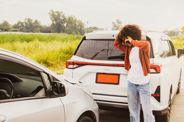 Frustrated african american woman looks at her own car on the road that has been hit and the rear of the car is damaged using smartphone to tell the insurance company to clear and assess the damage. - obrazy, fototapety, plakaty