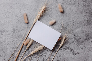 White invitation card mockup with dry flower on gray background