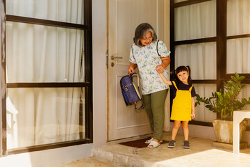 Retired grandmother carrying a student backpack carries her adorable little granddaughter, her...