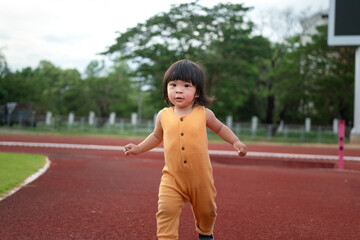 Fototapeta na wymiar Action of a little cute girl is enjoy running on the running track at soccer stadium with happy moment. People portrait photo in recreation activity.