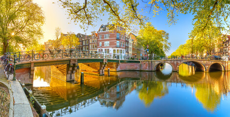 Panoramic view of Amsterdam in the morning sun. Traditional old houses, bridges and mirror water...
