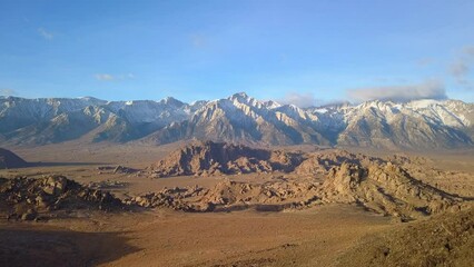 Aerial Descend Shot Of Rocky Landscape And Mountains Against Sky On Sunny Day - Alabama Hills, California