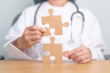 Doctor hand connecting couple puzzle piece, wooden jigsaw in hospital. Teamwork, Idea, Solution,...