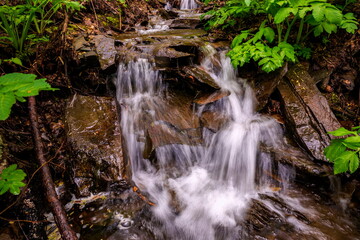Obraz premium picturesque waterfall on a stream running from the mountains along a ravine on a spring day