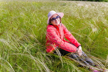 Naklejka na ściany i meble beautiful mature women sits in a flowering field of feather grass and enjoys nature