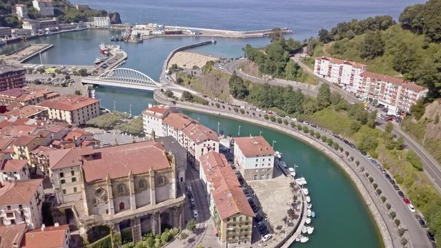 Aerial shot over the historic fishing town of Ondarroa, Spain. View over the meandering Artibai River. Flying over the Santa Maria Church, looking out to Ondarroa Port and beyond to the Bay of Biscay.