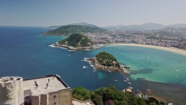 Aerial shot flying over the Monte Igeldo's Tower to Santa Clara Island situated in La Concha Bay.  In the background is the historic town of San Sebastian (Donostia), Spain on the Cantabrian Sea.