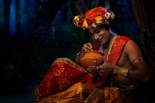 Young man dressed up as Lord Krishna eating makhan on the occasion of Janmashtami
