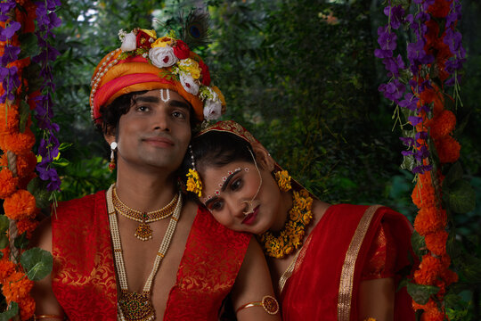 Young man and woman dressed up as Radha and Krishna and sitting together on a swing on the occasion of Janmashtami