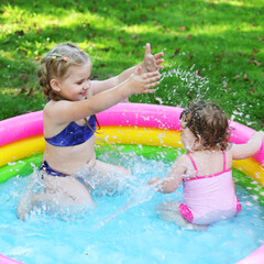 Children in the pool, it's hot in the summer. A little girl. A child plays in a children's pool. Swimming in the yard, inflatable pool in the shade. The girl loves water. Happy child in a swimsuit