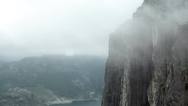 Impressive Timelapse of the Pulpit Rock, Preikestolen in Norway, A lot of Tourists are gathered on the Cliff, Cloudy Foggy Day, Mass Tourism in Bad Weather