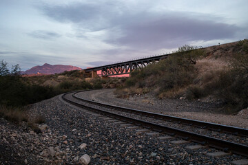 Train bridge going over train tracks at sunset - obrazy, fototapety, plakaty
