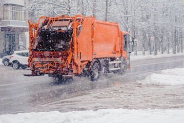 Orange recycling truck in motion on snowy city street during snowfall, Dynamic image: an orange...