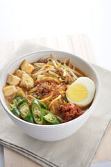 Malay mee rebus noodle with boiled egg, tofu, green chilli, sambal, vegetable, chilli sauce and hot thick spicy gravy soup in bowl on white background asian halal food cuisine menu for cafe design