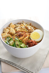 Malay mee rebus noodle with boiled egg, tofu, green chilli, sambal, vegetable, chilli sauce and hot thick spicy gravy soup in bowl on white background asian halal food cuisine menu for cafe design