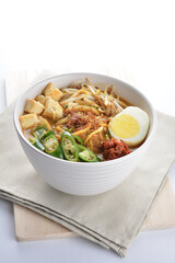 Malay mee rebus noodle with boiled egg, tofu, green chilli, sambal, vegetable, chilli sauce and hot thick spicy gravy soup in bowl on white background asian halal food cuisine menu for cafe design