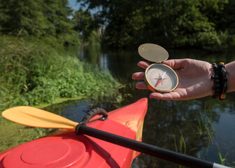 kompas trzymany w dłoni nad rzeką, w przerwie przeprawy kajakowej w słoneczny dzień - obrazy, fototapety, plakaty