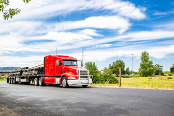 Bright red big rig semi truck tractor with loaded flat bed semi trailer standing on the road in...