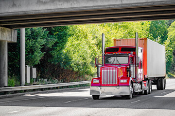 Classic American red big rig semi truck tractor with chrome parts transporting container on the...