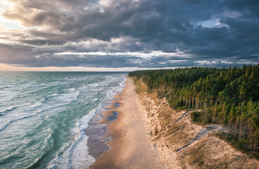 Fototapeta na wymiar Baltic sea in colorful sunset colors with storm clouds. Turquoise water with waves, and sandy coastline.