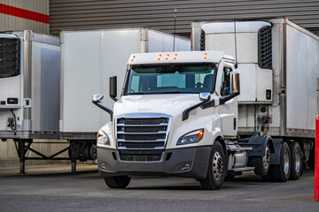 Day cab white big rig semi truck tractor with refrigerator semi trailer unloading delivered cargo...