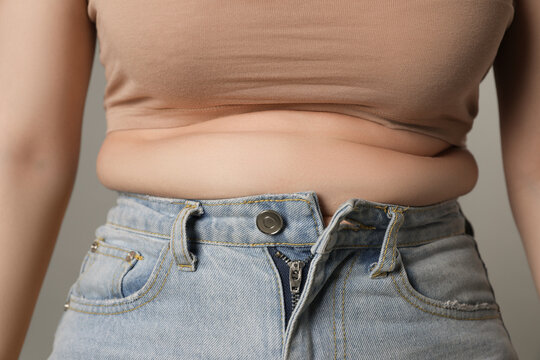Overweight woman in tight jeans on grey background, closeup