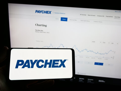 Stuttgart, Germany - 08-06-2023: Person holding mobile phone with logo of American outsourcing company Paychex Inc. on screen in front of web page. Focus on phone display.