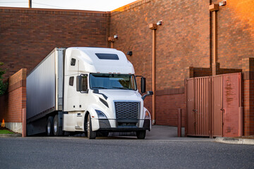 Industrial big rig white semi truck with dry van semi trailer unloading delivered cargo standing in...