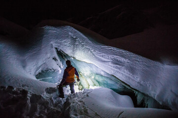 Silhouetted high angle of climber entering ice cave at night