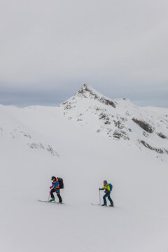 Two men on skis skinning up with remote mountain peak behind