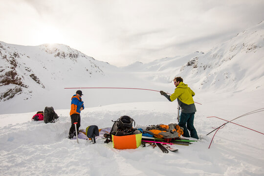 Two men set up tent on snow in remote mountain location