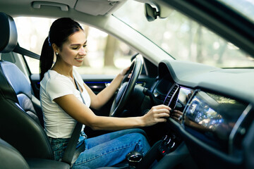 Woman amateur driver is playing the radio in the car before start driving.