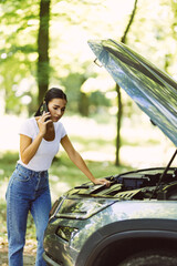 Young woman standing by broken car on the road and using smartphone calling assistance.