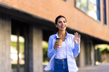 Smiling young woman with coffee waving her hand with a friendly cheerful smile to her neighbours.