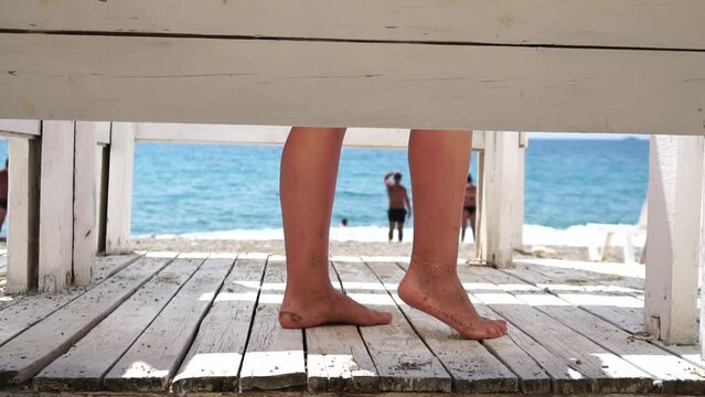 Woman in the changing, dressing room on beach, at sunset on the seashore. Close-up of bare female feet legs in enclosed changing room cabin. Summer holiday vacation and travel concept. Slow motion
