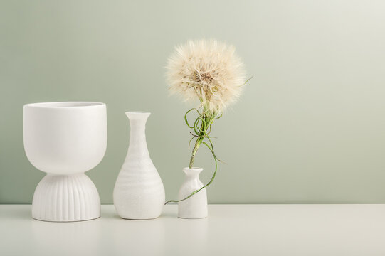 Three ceramic vases and a large dandelion on a white table against an olive wall.