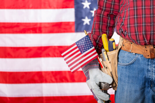 Carpenter in protective gloves and toolbelt with us flag labor day background