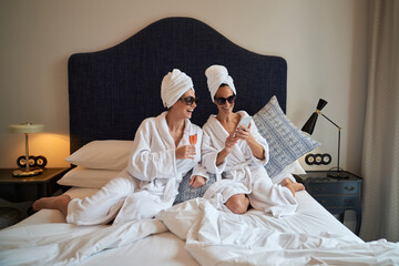 Positive female friends resting on bed in holiday morning