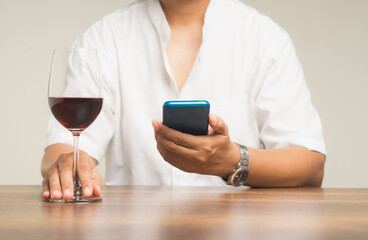 Close-up of hands holding a glass of red wine and a smartphone while sitting at the table.