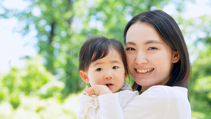 新緑の前で赤ちゃんを抱っこするママ