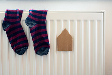 Paper house and pair of colored socks on the white radiator. Housing, energy, economy, domestic theme