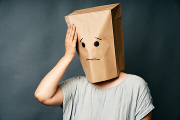 Woman with hand on head and upset smile on the paper bag on head
