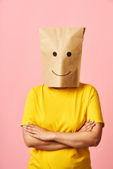Confident young woman in smiling paper bag on head and crossed arms over pink background
