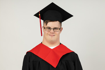 Smiling young man with cerebral palsy wearing glasses in a graduate suit. World Genetic Diseases Day concept