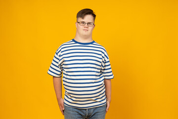 Smiling young man with cerebral palsy in glasses in a striped t-shirt on a yellow background. World...