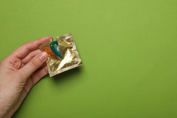 Open package with condom in hand on green background, place for text